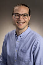 Douglas Lischke, DO, a white man with glasses, poses for a headshot wearing a light blue button down shirt.