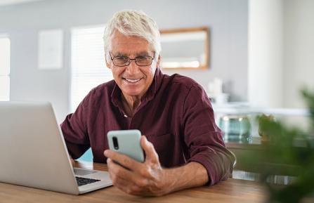 Man using a mobile phone while sitting in front of a computer.