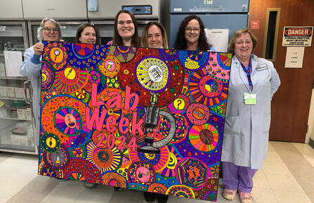 A group of medical lab professionals hold up a colored banner