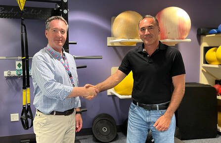Physical therapist Jim Hall shakes hands with patient Steve Walsh in an exercise room with purple walls