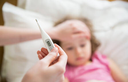 A child laying in bed while an adult takes their temperature