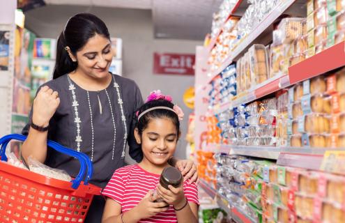 Mother and daughter shop with a basket as a daughter reads the label on a jar