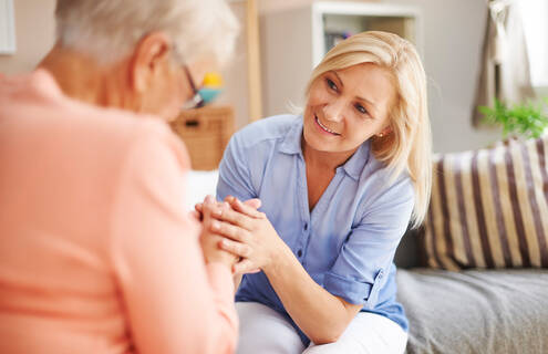 A blonde woman holds the hand of an older woman, presumably her mother