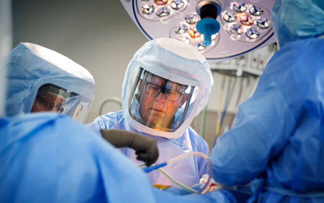 A team of surgeons in protective gear is engaged in a surgical procedure in a well-lit operating room, focusing intently on their work.