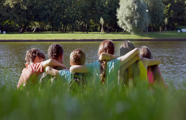 A group of children embrace while looking over a lake