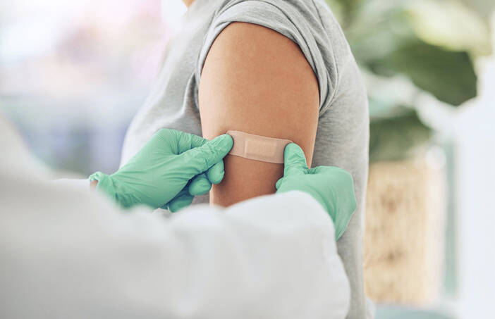 Image of person's arm with a medical professional wearing gloves preparing to administer a flu shot